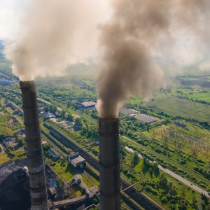 Industrielle skorstene, der udleder røgfaner over et landligt landskab.