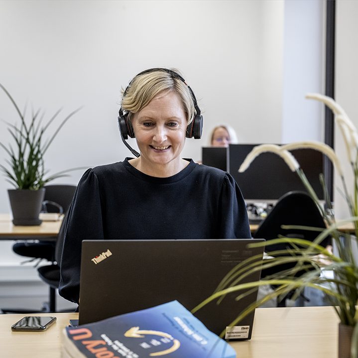 Billede af kvinde der sidder foran sin bærbar med hovedtelefoner på.