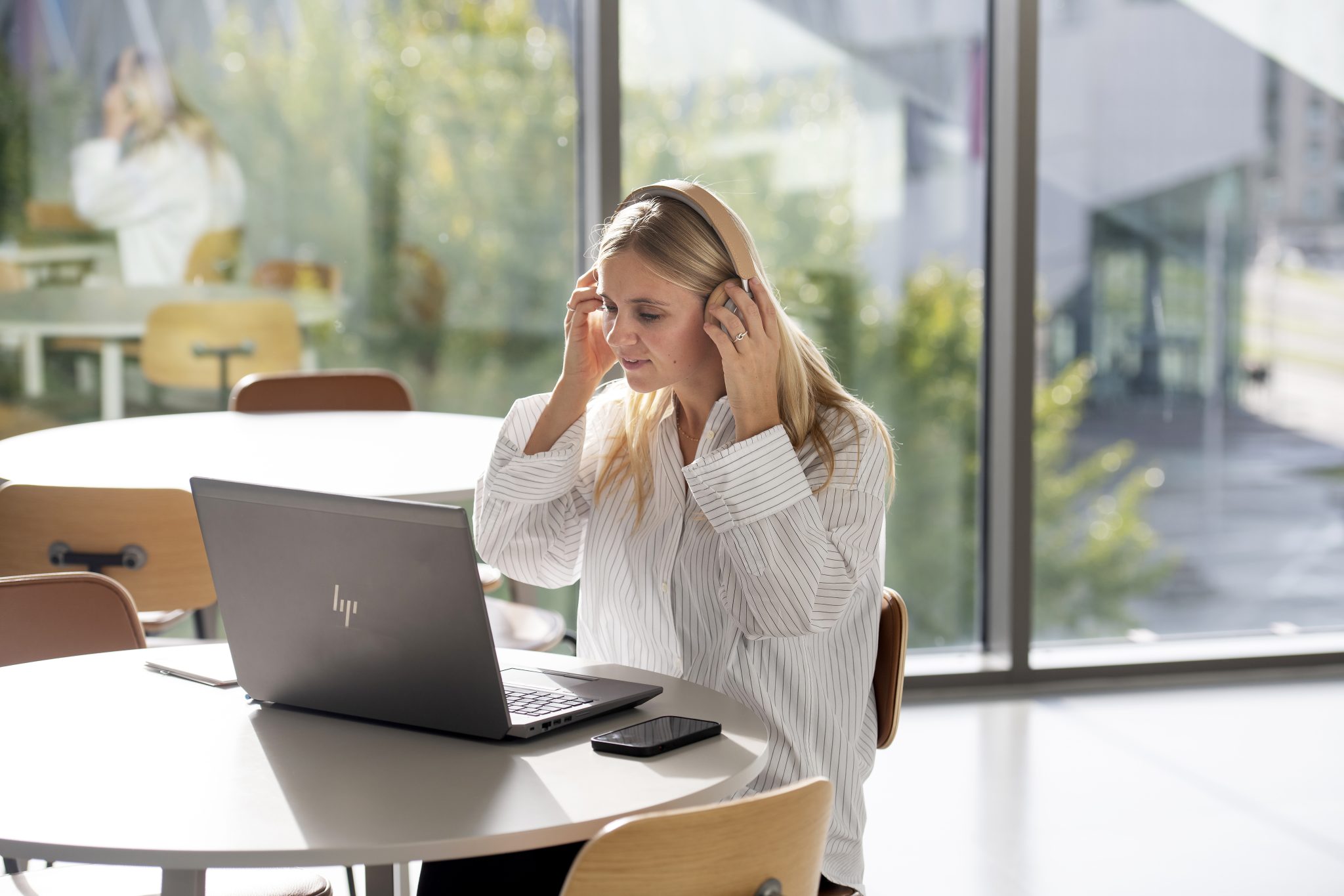 Billede af ung kvinde, der tager sine høretelefoner på, mens hun sidder med sin bærbar computer.