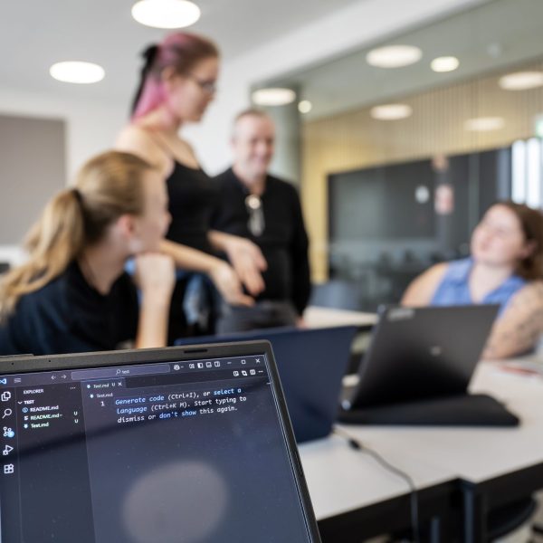 Unge mennesker der sidder og snakker, mens der er en computer i forgrunden.