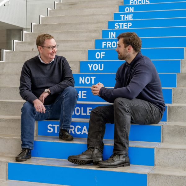 Underviser og studerende, der sidder på en trappe og snakker.