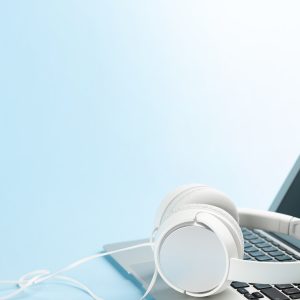 White headphones and laptop over blue background with copy space. Podcast, audiobook or music template